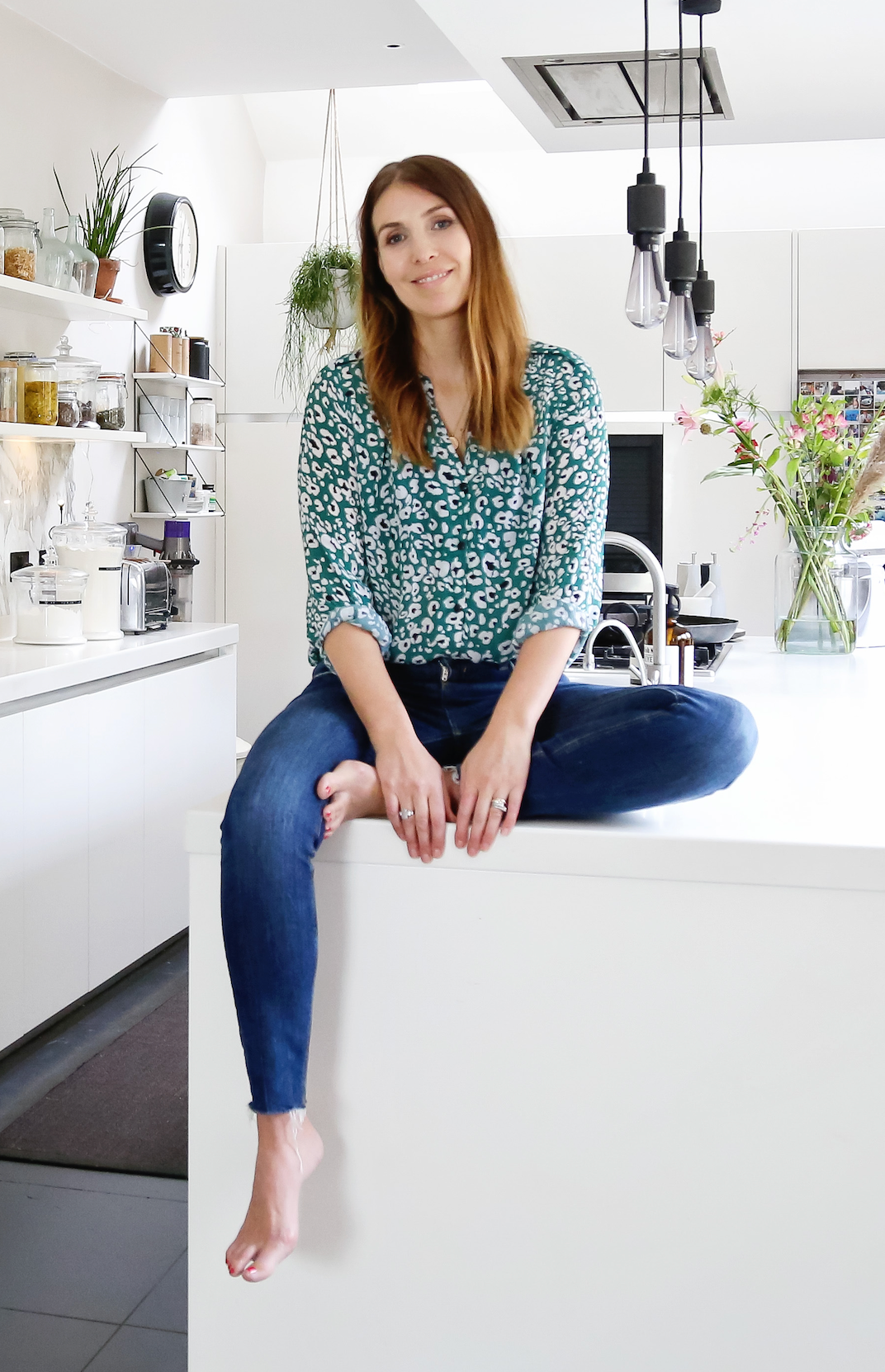 Izzy seated in her kitchen, with herbs and flowers around her